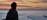 Person meditating cross-legged on a beach shoreline at sunrise - calm golden light for wellness